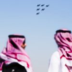 
              Arab men watch as the Russian Knights perform a stunt at the Dubai Air Show in Dubai, United Arab Emirates, Sunday, Nov. 14, 2021. The biennial Dubai Air Show opened Sunday as commercial aviation tries to shake off the coronavirus pandemic. (AP Photo/Jon Gambrell)
            