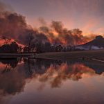 Smoke from the Pilot Mountain State Park wildfire is reflected in a private pond east of the park at sunset, Monday, Nov. 29, 2021, in North Carolina. The fire, which was reported to have started Saturday, has burned more than 500 acres as of Monday night and is expected to burn more as foresters set back fires to protect houses below the mountain. (Walt Unks/The Winston-Salem Journal via AP)