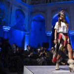 
              A model takes to the catwalk inside the 19th century building City Hall in Sarajevo, Bosnia, Thursday, Dec. 16, 2021, during the presentation of a collection dubbed "No Nation Fashion", a migrant-made fashion brand project. At the fashion show migrant models came out on the catwalks in designs meant to symbolize various stages of their journeys _ the 'nomadic' road away from home and the transit to new lives in new countries while the panel in the background read "We are strong," and "We smile." (AP Photo)
            