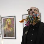 
              Artist Lynx Alexander, of New York, wears a protective face mask made of fabric butterflies and other materials as he views art displayed at Art Miami during Miami Art Week, Wednesday, Dec. 1, 2021, in Miami. Miami Art Week is an annual event centered around the Art Basel Miami Beach fair. (AP Photo/Lynne Sladky)
            