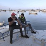 
              Ziad Khaled Hilweh, right, and his friend Bilal Mousa, who tried to migrate to Europe, speak as they sit in a boat, at a port in the northern city of Tripoli, Lebanon, Monday, Dec. 6, 2021. Lebanese are setting off from the port city of Tripoli to attempt the perilous journey by boat to Cyprus and beyond in the hopes of reaching Europe. They are joining Iraqis, Afghans and Sudanese in leaving their homeland after Lebanon's economic collapse has thrown two-thirds of the population into poverty in just over a year. (AP Photo/Bilal Hussein)
            