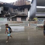 
              Locals walk past destroyed buildings in Honiara, Solomon Islands, Monday, Dec. 6, 2021. Lawmakers in the Solomon Islands are debating whether they still have confidence in the prime minister, after rioters last month set fire to buildings and looted stores in the capital.(Gary Ramage via AP)
            