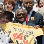 FILE - Bishop Desmond Tutu of South Africa displays an "End Apartheid" T-shirt at New York's City Hall, May 27, 1986. South Africa's president says Desmond Tutu, South Africa's Nobel Peace Prize-winning activist for racial justice and LGBT rights and the retired Anglican Archbishop of Cape Town, has died at the age of 90, it was announced on Sunday, Dec. 26, 2021. An uncompromising foe of apartheid, South Africa's brutal regime of oppression again the Black majority, Tutu worked tirelessly, but non-violently, for its downfall. (AP Photo/Susan Ragan, File)