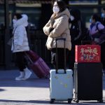 
              A traveler waits outside the Beijing railway station with her trolley bags and a gift box with the words "The taste of New Year" in Beijing, China, Friday, Jan. 28, 2022. The Beijing Winter Olympics is coinciding with the Chinese Lunar New Year and renewed Covid outbreaks prompting the Chinese authorities to call on the public to stay where they are instead of traveling to their hometowns for the year's most important family holiday. (AP Photo/Ng Han Guan)
            