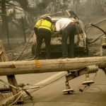 
              FILE - In this Nov. 10, 2018 file photo, with a downed power utility pole in the foreground, Eric England, right, searches through a friend's vehicle after the wildfire burned through Paradise, Calif. The nation's largest utility, Pacific Gas & Electric is poised to emerge from five years of criminal probation amid worries that it remains too dangerous to be trusted. Over the five years, the utility became an even more destructive force. More than 100 people have died and thousands of homes and businesses have been incinerated in wildfires sparked by its equipment in that time. (AP Photo/Noah Berger, File)
            