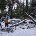 
              A couple walks past a fallen tree on a parked vehicle, in Athens, after a snowstorm on Tuesday, Jan. 25, 2022. A snowstorm of rare severity disrupted road and air traffic Monday in the Greek capital of Athens and neighboring Turkey's largest city of Istanbul, while most of Greece, including — unusually — several Aegean islands, and much of Turkey were blanketed by snow. (AP Photo/Thanassis Stavrakis)
            