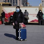 
              A traveler waits outside the Beijing railway station with her suitcase in Beijing, China, Friday, Jan. 28, 2022. The Beijing Winter Olympics is coinciding with the Chinese Lunar New Year and renewed Covid outbreaks prompting the Chinese authorities to call on the public to stay where they are instead of traveling to their hometowns for the year's most important family holiday. (AP Photo/Ng Han Guan)
            
