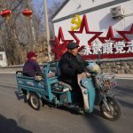 
              Local residents past by a sign which reads "Forever follow the Communist Party" at Houheilong Miao, a village in Yanqing on the outskirts of Beijing, China, Wednesday, Jan. 5, 2022. The village has a view of the Olympics skiing venue in the distance. Its 20 mostly vacant traditional courtyard houses have been turned into lodgings and a cafe dubbed the "Winter Olympic Home." (AP Photo/Ng Han Guan)
            