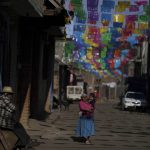
              Residents walk along a street decorated with elaborately cut colored pieces of tissue paper called “papel picado, in the Puerpecha Indigenous community of Comachuen, Mexico, Wednesday, Jan. 19, 2022. In some places in rural Mexico, like Comachuen, remittances are often the lifeblood of many towns. Every store, business and family in Comachuen depends on remittances. (AP Photo/Fernando Llano)
            
