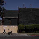 
              A woman walks her dog past the Jefferson oil drill site enclosed by tall fences in Los Angeles, Wednesday, June 2, 2021. Los Angeles, the second most populous city in the United States, is weighing whether to ban new oil and gas drilling and phase out existing wells. The city council is expected to vote on a measure that would shut down oil and gas fields in the city after a decade of complaints from residents. (AP Photo/Jae C. Hong)
            