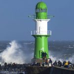 
              People stand near the lighthouse on the pier of Warnemunde in stormy weather in Rostock, Germany on Sunday Jan. 30, 2022. (Jens Buttner/dpa via AP)
            