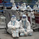 
              Olympic workers in protective clothing rest after they helped travelers at the Beijing Capital International airport after the 2022 Winter Olympics, Monday, Feb. 21, 2022, in Beijing, China. (AP Photo/Frank Augstein)
            