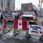 
              Signs sit on a barricade in front of parked vehicles as part of the trucker protest, Tuesday, Feb. 8, 2022 in Ottawa's downtown core. Canadian lawmakers expressed increasing worry about protests over vaccine mandates other other COVID restrictions  after the busiest border crossing between the U.S. and Canada became partially blocked.  (Adrian Wyld /The Canadian Press via AP)
            