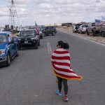 
              A supporter walks past cars as they join the trucker caravan to Washington, D.C., called The People's Convoy Wednesday, Feb. 23, 2022, in Adelanto, Calif. A small convoy of truckers demanding an end to coronavirus mandates began a cross-country drive from California to the Washington, D.C., area on Wednesday. (AP Photo/Nathan Howard)
            