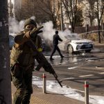 
              Ukrainian soldiers take positions outside a military facility as two cars burn, in a street in Kyiv, Ukraine, Saturday, Feb. 26, 2022. Russian troops stormed toward Ukraine's capital Saturday, and street fighting broke out as city officials urged residents to take shelter. (AP Photo/Emilio Morenatti)
            
