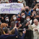 
              Pope Francis puts on a skull cap he was just presented with as he walks by a placard in Italian reading : "Today is my birthday", at the end of his weekly general audience in the Paul VI Hall at the Vatican, Wednesday, Feb. 02, 2022. (AP Photo/Gregorio Borgia)
            