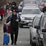 
              Ukrainian refugees walk along vehicles lining-up to cross the border from Ukraine into Moldova, at Mayaky-Udobne crossing border point near Udobne, Ukraine, Saturday, Feb. 26, 2022. The U.N. refugee agency says nearly 120,000 people have so far fled Ukraine into neighboring countries in the wake of the Russian invasion. The number was going up fast as Ukrainians grabbed their belongings and rushed to escape from a deadly Russian onslaught. (AP Photo/Sergei Grits)
            