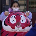 
              A child wearing a mask holds on to the ears of a Tiger sculpture on the first day of the Lunar Year of the Tiger in Beijing, China, Tuesday, Feb. 1, 2022. (AP Photo/Ng Han Guan)
            