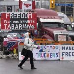 
              A woman crosses the street in front of vehicles parked as part of the trucker protest,  Tuesday, Feb. 8, 2022 in Ottawa.  Canadian lawmakers expressed increasing worry about protests over vaccine mandates other other COVID restrictions  after the busiest border crossing between the U.S. and Canada became partially blocked.   (Adrian Wyld /The Canadian Press via AP)
            