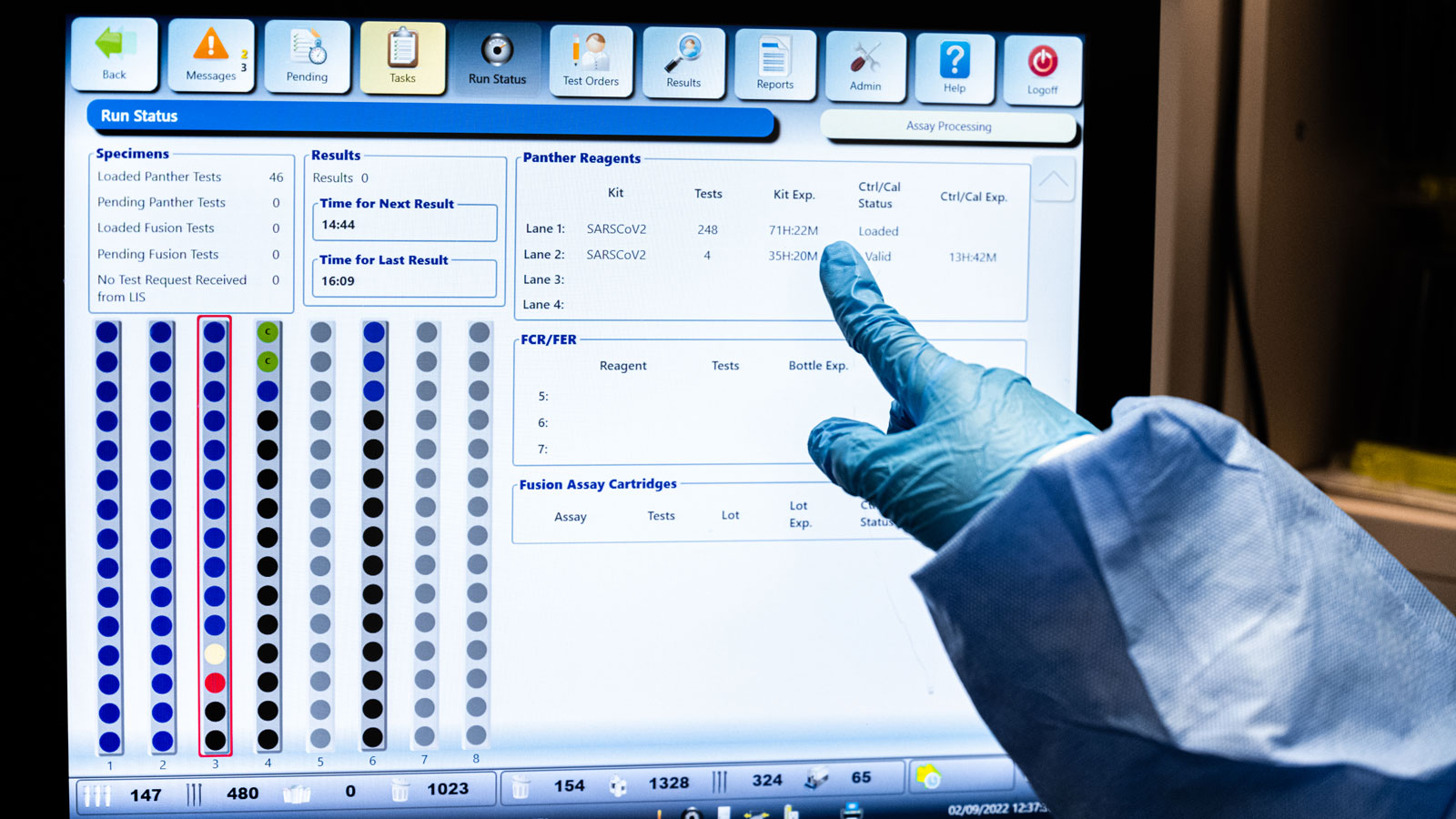 The gloved hand of Deira Ward, a medical technologist, points toward the display screen of a PCR an...