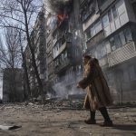
              A woman walks past a burning apartment building after shelling in Mariupol, Ukraine, Sunday, March 13, 2022. (AP Photo/Evgeniy Maloletka)
            