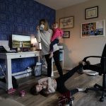 
              Tara Carpenter holds Alyssa Carpenter, 2, as Hailey Carpenter, 9, plays at her feet and Audrey Carpenter, 5, sits left, as she ties to work in her home office in Haymarket, Va., Friday, Jan. 28, 2022. Alyssa has had COVID-19 twice and suffers long-term symptoms. All three girls are part of a NIH-funded multi-year study at Children's National Hospital to look at impacts of COVID-19 on children's physical health and quality of life. (AP Photo/Carolyn Kaster)
            