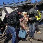 
              Volunteers pass an improvised path under a destroyed bridge as they evacuate an elderly resident in Irpin, some 25 km (16 miles) northwest of Kyiv, Friday, March 11, 2022. Kyiv northwest suburbs such as Irpin and Bucha have been enduring Russian shellfire and bombardments for over a week prompting residents to leave their home. (AP Photo/Efrem Lukatsky)
            