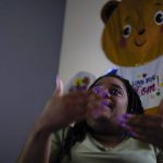 
              Danielle Mitchell talks about her daughter, Brooklynn Chiles, 8, in her bedroom home office in Washington, Wednesday, Feb. 9, 2022. Brooklynn's father, Rodney Chiles, died of COVID-19 last year and Brooklynn has tested positive three times. She is part of a NIH-funded multi-year study at Children's National Hospital to look at impacts of COVID-19 on children's physical health and quality of life. (AP Photo/Carolyn Kaster)
            