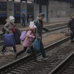
              A family runs over the tracks trying to board a Lviv bound train, in Kyiv, Ukraine, Thursday, March 3, 2022. Ukrainian President Volodymyr Zelenskyy's office says a second round of talks with Russia aimed at stopping the fighting that has sent more than 1 million people fleeing over Ukraine's borders, has begun in neighboring Belarus, but the two sides appeared to have little common ground. (AP Photo/Vadim Ghirda)
            