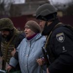 
              Ukrainian police officers help a woman fleeing as the artillery echoes nearby in Irpin, in the outskirts of Kyiv, Ukraine, Monday, March 7, 2022. (AP Photo/Emilio Morenatti)
            