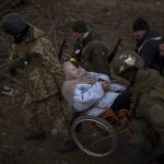 
              Ukrainian soldiers and militiamen carry a woman in a wheelchair as the artillery echoes nearby, while people flee Irpin on the outskirts of Kyiv, Ukraine, Monday, March 7, 2022. Russia announced yet another cease-fire and a handful of humanitarian corridors to allow civilians to flee Ukraine. Previous such measures have fallen apart and Moscow's armed forces continued to pummel some Ukrainian cities with rockets Monday. (AP Photo/Emilio Morenatti)
            