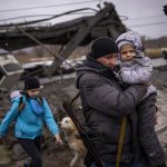 
              Local militiaman Valery, 37, carries a child as he helps a fleeing family across a bridge destroyed by artillery, on the outskirts of Kyiv, Ukraine, Wednesday, March 2. 2022. Russian forces have escalated their attacks on crowded cities in what Ukraine's leader called a blatant campaign of terror. (AP Photo/Emilio Morenatti)
            
