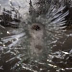
              A man is seen through a bullet hole of a machine-gunned bus after an ambush in the city of Kyiv, Ukraine, Friday, March 4, 2022. While a small group of reservists were burying their comrade, 54-year-old Volodymyr Nezhenets, who was one of three killed on Feb. 26 in an ambush Ukrainian authorities say was caused by Russian 'saboteurs', a few kilometers away from the cemetery, the remains of the convoy Volodymyr was killed in 6 days ago still stands in the road with charred vehicles, a bus riddled with bullets, a spatter of blood on the drivers seat. (AP Photo/Emilio Morenatti)
            