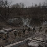 
              Foreign and Ukrainian soldiers cross an improvised path under a destroyed bridge in Irpin, outskirts of Kyiv, Ukraine, Saturday, March 12, 2022. Kyiv northwest suburbs such as Irpin and Bucha have been enduring Russian shellfire and bombardments for over a week prompting residents to leave their homes. (AP Photo/Felipe Dana)
            