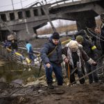 
              Local militiamen help an old woman crossing a bridge destroyed by artillery, as she tries to flee, on the outskirts of Kyiv, Ukraine, Wednesday, March 2. 2022. Russian forces have escalated their attacks on crowded cities in what Ukraine's leader called a blatant campaign of terror. (AP Photo/Emilio Morenatti)
            