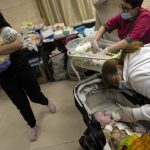 
              A worker feeds a newborn baby in a basement converted into a nursery in Kyiv, Ukraine, Saturday, March 19, 2022. Nineteen surrogated babies were born to surrogate mothers, with their biological parents still outside the country due to the war against Russia. (AP Photo/Rodrigo Abd)
            