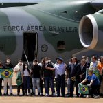 
              Brazil's President Jair Bolsonaro and his ministers pose for a group photo on the tarmac of an air force base, with dozens of Brazilians, along with about 20 Ukrainian citizens and a handful of other Latin Americans stranded in Ukraine, in Brasilia, Brazil, Thursday, March 10, 2022. The passengers were transported by a Brazilian Air Force plane from Poland. Brazil has pledged to repatriate its citizens from the war zone, and has offered Ukrainian refugees asylum in the country. (AP Photo/Eraldo Peres)
            