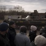 
              Residents lining up for aid watch as Ukrainian soldiers ride atop a tank in the town of Trostsyanets, Ukraine, Monday, March 28, 2022. Trostsyanets was recently retaken by Ukrainian forces after being held by Russians since the early days of the war. (AP Photo/Felipe Dana)
            