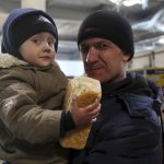 
              A man and his child look at a photographer as they wait to get a food and drinking water at a supermarket on the territory which is under the Government of the Donetsk People's Republic control, on the outskirts of Mariupol, Ukraine, Thursday, March 24, 2022. (AP Photo/Alexei Alexandrov)
            