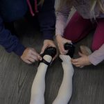 
              Alyssa Carpenter, 2, is helped into tap shoes by her mother, Tara Carpenter,, left, and big sister Audrey Carpenter, 5, right, during Tiny Tot ballet and tap class at Lyrique Dance in Warrenton, Va., Saturday, Jan. 15, 2022. Alyssa has had COVID-19 twice and suffers long-term symptoms. She had a fever before dance class this morning. She and her two sisters are part of a NIH-funded multi-year study at Children's National Hospital to look at impacts of COVID-19 on children's physical health and quality of life. (AP Photo/Carolyn Kaster)
            