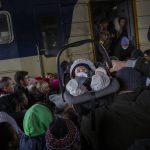 
              A man carries a baby as people crowd as they try to get on a train to Lviv at the Kyiv station, Ukraine, Friday, March 4. 2022. Ukrainian men have to stay to fight in the war while women and children are leaving the country to seek refuge in a neighboring country. (AP Photo/Emilio Morenatti)
            