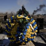 
              A smoke from shelling rises as a wreath of flowers is placed at a cemetery in Vasylkiv south west of Kyiv, Ukraine, Saturday, March 12, 2022. Russian forces appeared to make progress from northeast Ukraine in their slow fight to reach the capital, Kyiv, while tanks and artillery pounded places already under siege. (AP Photo/Vadim Ghirda)
            