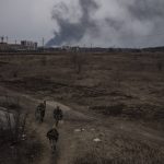 
              Soldiers walk on a path as smoke billows from the town of Irpin, on the outskirts of Kyiv, Ukraine, Saturday, March 12, 2022. Kyiv northwest suburbs such as Irpin and Bucha have been enduring Russian shellfire and bombardments for over a week prompting residents to leave their homes. (AP Photo/Felipe Dana)
            