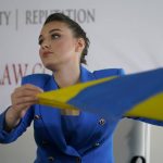 
              CORRECTS SPELLING OF FIRST NAME TO VERONIKA, NOT VERONICA -  Veronika Didusenko, Miss Ukraine 2018, who was forced to flee from Ukraine with her 7-year-old son, holds the Ukrainian national flag at a news conference at women’s rights attorney Gloria Allred's office in Los Angeles, Tuesday, March 8, 2022. Didusenko and her son fled the country on Feb. 24, 2022, when Russia began to bomb Kyiv, their home city. (AP Photo/Damian Dovarganes)
            