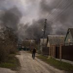 
              A Ukrainian man rides his bicycle near a factory and a store burning after it had been bombarded in Irpin, on the outskirts of Kyiv, Ukraine, Sunday, March 6, 2022. (AP Photo/Emilio Morenatti)
            