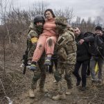 
              A woman carried by Ukrainian soldiers crosses an improvised path while fleeing the town of Irpin, Ukraine, Sunday, March 6, 2022. In Irpin, near Kyiv, a sea of people on foot and even in wheelbarrows trudged over the remains of a destroyed bridge to cross a river and leave the city. (AP Photo/Oleksandr Ratushniak)
            