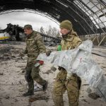 
              Ukrainian sappers carry a Russian military drone backdropped by the Antonov An-225, world's biggest cargo aircraft destroyed by the Russian troops during recent fighting, at the Antonov airport in Hostomel, on the outskirts of Kyiv, Ukraine, Monday, April 18, 2022. (AP Photo/Efrem Lukatsky)
            