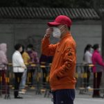 
              A volunteer wearing a red cap adjusts his mask as residents line up for mass COVID test, Wednesday, April 27, 2022, in Beijing. Workers put up fencing and police restricted who could leave a locked-down area in Beijing on Tuesday as authorities in the Chinese capital stepped up efforts to prevent a major COVID-19 outbreak like the one that has all but shut down the city of Shanghai. (AP Photo/Ng Han Guan)
            