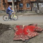 
              FILE - A man rides his bicycle past a body covered by a rug after fighting on the outskirts of Mariupol, Ukraine, in territory under control of the separatist government of the Donetsk People's Republic, on Tuesday, March 29, 2022. (AP Photo/Alexei Alexandrov, File)
            