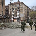 
              Servicemen of Donetsk People's Republic militia walk past damaged apartment buildings near the Illich Iron & Steel Works Metallurgical Plant, the second largest metallurgical enterprise in Ukraine, in an area controlled by Russian-backed separatist forces in Mariupol, Ukraine, Saturday, April 16, 2022. Mariupol, a strategic port on the Sea of Azov, has been besieged by Russian troops and forces from self-proclaimed separatist areas in eastern Ukraine for more than six weeks. (AP Photo/Alexei Alexandrov)
            